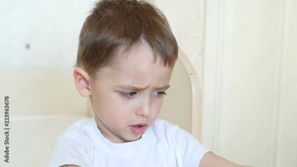 Emotions of the child: the boy shows discontent, sitting at the table. Emotions of the child: the boy shows discontent, sitting at the table.
