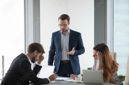 Angry male worker standing talking to colleagues lecturing on mistake in documents or failed project, businessman show dissatisfaction to business partner during negotiations or meeting in office photo