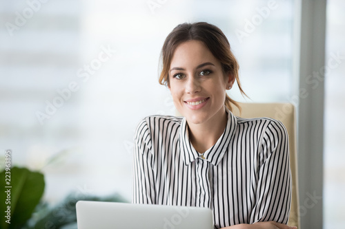 Portrait of smiling beautiful millennial businesswoman or CEO looking at camera, happy female boss posing making headshot picture for company photoshoot, confident successful woman at work photo