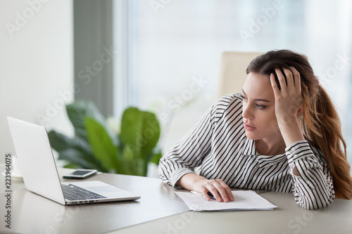 Bored millennial female worker lie at office desk look at laptop screen think about problem solution, unmotivated businesswoman search inspiration, tired of monotonous work. Lack of motivation concept