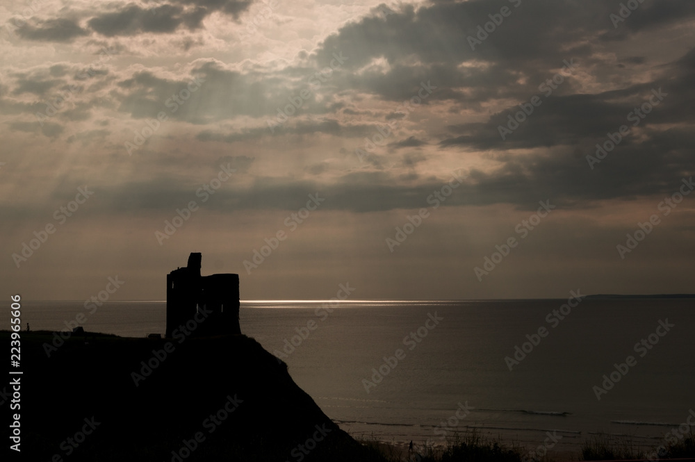 silhouette of a castle with background of orange overcast sky and sun rays
