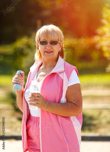Pensioner woman sport. Adult woman is engaged in outdoor sports. Sport woman holding dumbbells and bottle of water. Active lifestyle. Happy woman. © A Stock Studio