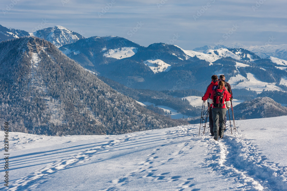 Wanderer mit roten Jacken im Schnee mit Schatten und Ausblick auf die Berge, Bayern