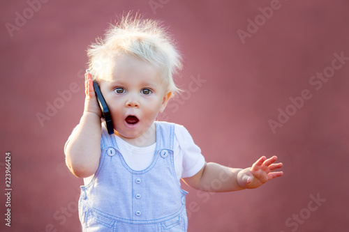 Cute baby boy playing with mobile phone in the park, digital technologies in the hands of a child