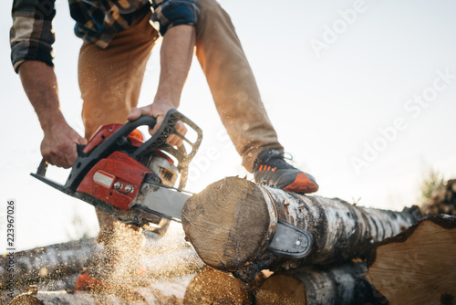 Professional lumberman sawing trees on sawmill. Close-up view on chainsaw in hands photo