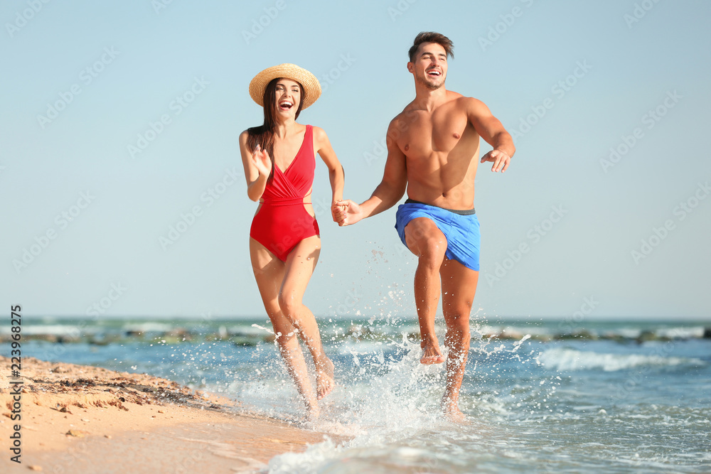 Happy young couple having fun at beach on sunny day - obrazy, fototapety, plakaty 