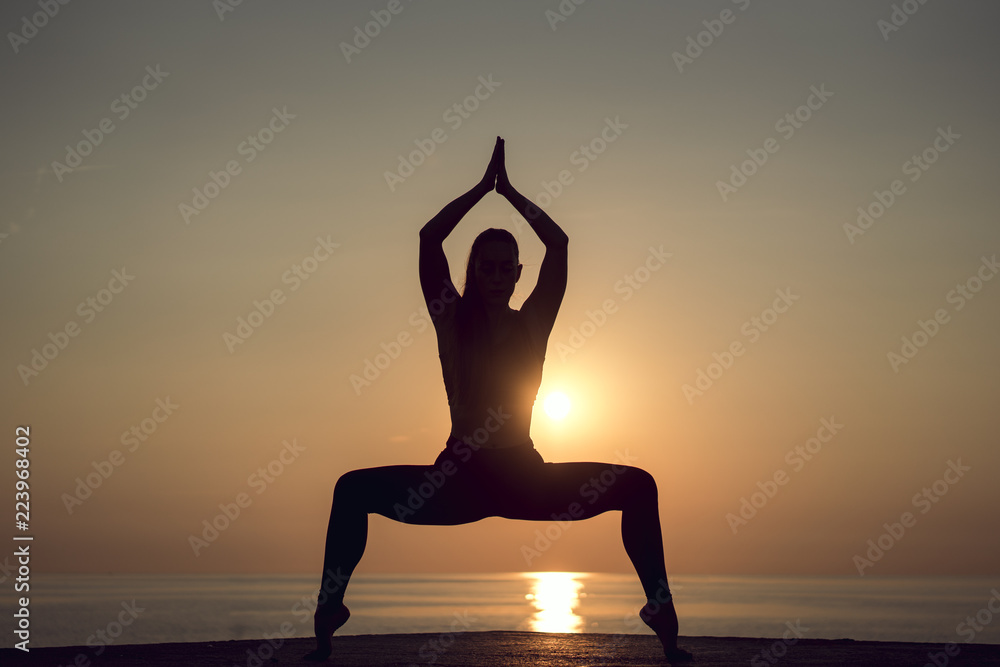 Rare view of silhouette of a woman, standing in a yoga pose while practicing meditation on tranquil beach at sunrise in the morning during summer vacation in Spain. Healthy lifestyle and relaxation.