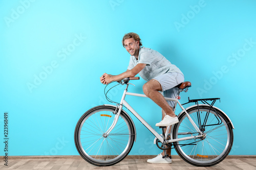 Fototapeta Naklejka Na Ścianę i Meble -  Handsome man with bicycle against color wall. Space for text