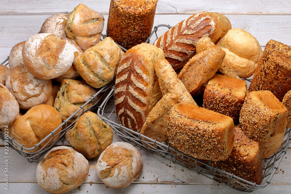 Different types of bread and buns in a metal basket on a wooden background