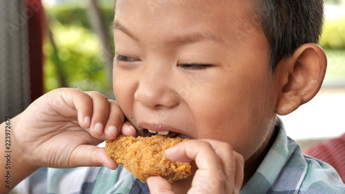Cute asian boy are happy eating fried chicken leg in restaurant