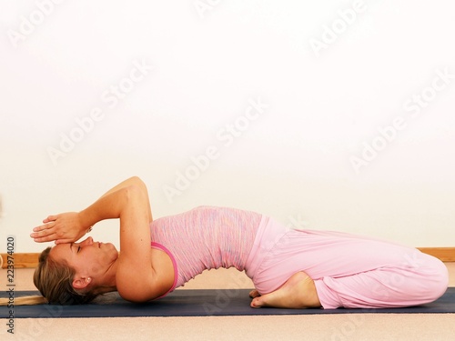 Young beautiful woman doing yoga pose, indoors, white background, wearing pink top