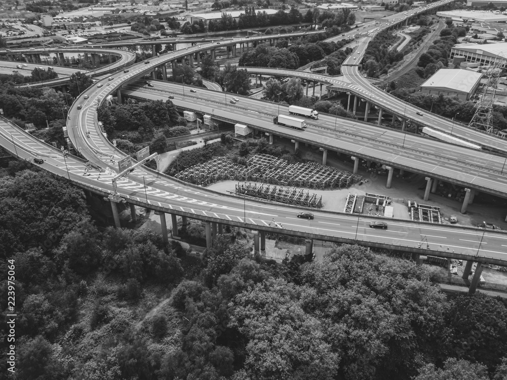 Aerial view of a complex motorway road junction with traffic moving. Cars, lorries, vans and a train can be seen travelling through a busy road interchange from above