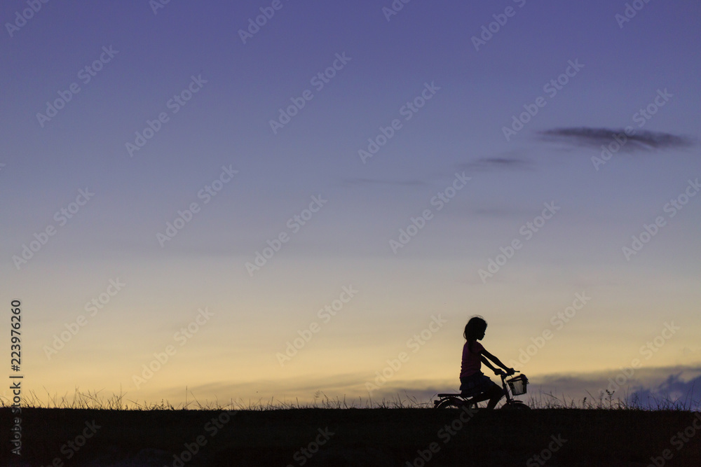 A silhouette photo of a girl riding bicycle in the park at sunset.
