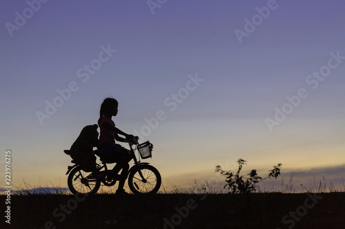 A silhouette photo of a girl riding bicycle in the park at sunset.