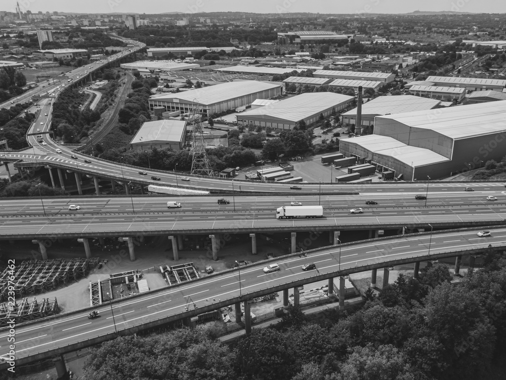 Aerial view of a complex motorway road junction with traffic moving. Cars, lorries, vans and a train can be seen travelling through a busy road interchange from above