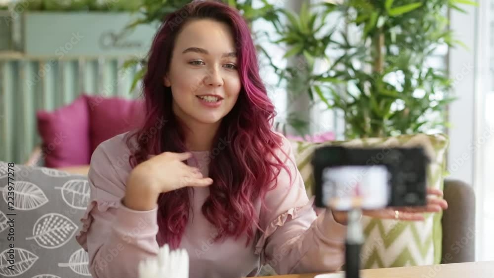 Young attractive female blogger with pink fashion hair blogging in cafe. Happy smiling woman with camera recording video tells about life, lifestyle. Technology, videoblog, mass media concept. Young attractive female blogger with pink fashion hair blogging in cafe. Happy smiling woman with camera recording video tells about life, lifestyle. Technology, videoblog, mass media concept.