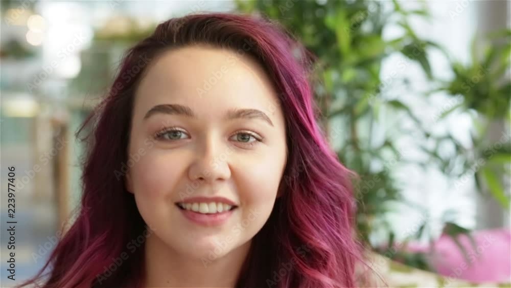 Close-up of attractive young teenage girl with pink hair smiling at camera and tell about her make up. Portrait of woman blogger recording selfie video