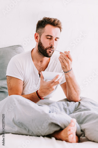 Young man eating breakfast in bed