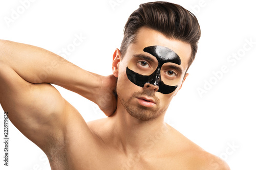 Young guy with a black charcoal mask on his face on white background.
