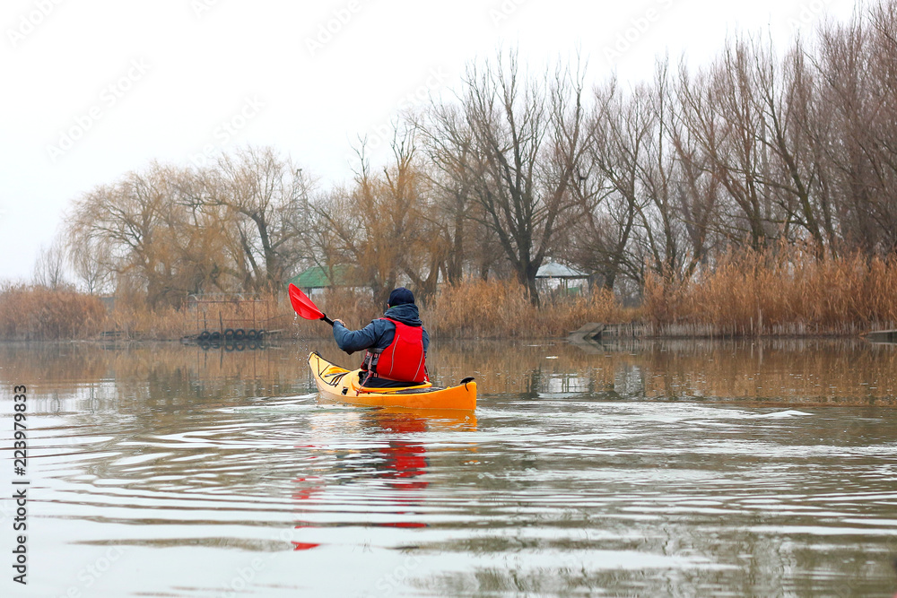 Man in the yellow kayak rowing on the river on a cloudy calm autumn day
