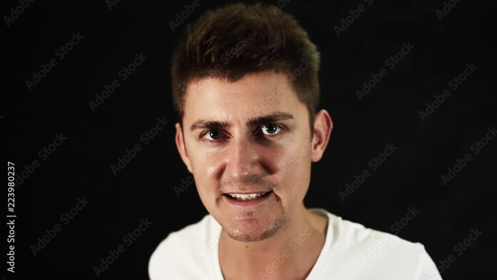 Face of beautiful young man with cute big blue eyes and modern haircut wearing white t-shirt who is emotionally singing in front of camera in room with black matte background. Face of beautiful young man with cute big blue eyes and modern haircut wearing white t-shirt who is emotionally singing in front of camera in room with black matte background.