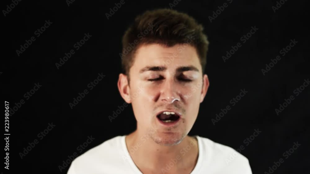 Portrait of young attractive, caucasian guy with cute big, blue eyes and modern haircut wearing white t-shirt who is emotionally singing in front of camera in room with black matte background. Portrait of young attractive, caucasian guy with cute big, blue eyes and modern haircut wearing white t-shirt who is emotionally singing in front of camera in room with black matte background.