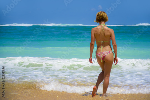 back portrait of young attractive woman in bikini looking at horizon at beautiful desert beach enjoying Summer holidays travel destination in relaxing tropical paradise