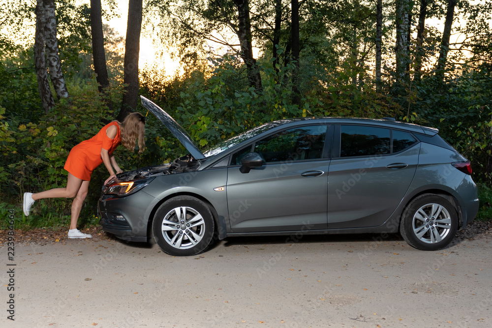 a young girl stands at a broken car and looks at the engine, does not understand how to repair a young girl stands at a broken car and looks at the engine, does not understand how to repair