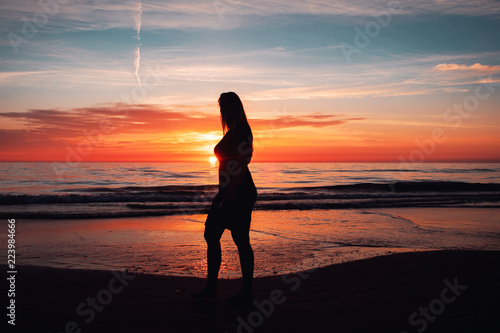 Silhouette portrait young woman walking on beach during sunset enjoying a summer evening at the beach