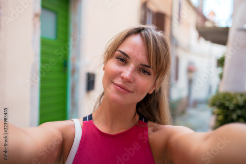 Young smiling woman taking selfie on narrow street during vacation in Croatia Free Download Young smiling woman taking selfie on narrow street during vacation in Croatia - GFXLoad