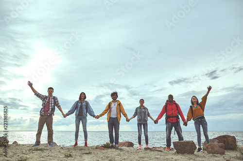 Gather together. Full length portrait of cheerful friends holding hands on the beach and smiling