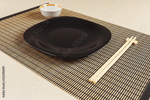 Oriental dishes and chopsticks on a bamboo mat.