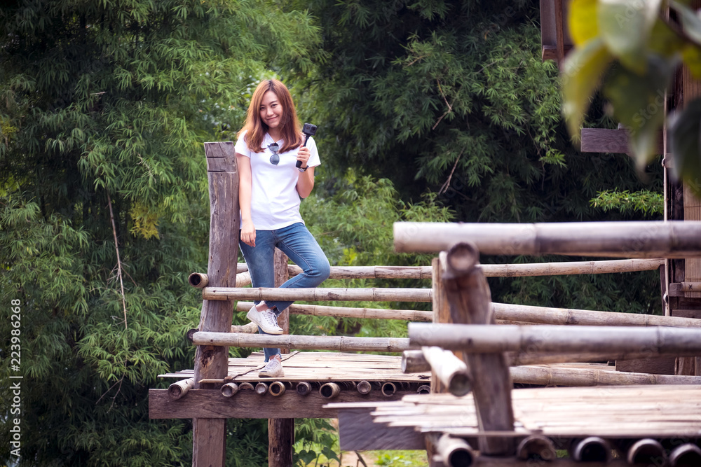 Naklejka premium A beautiful asian woman standing on wooden balcony in front of a house with green nature background