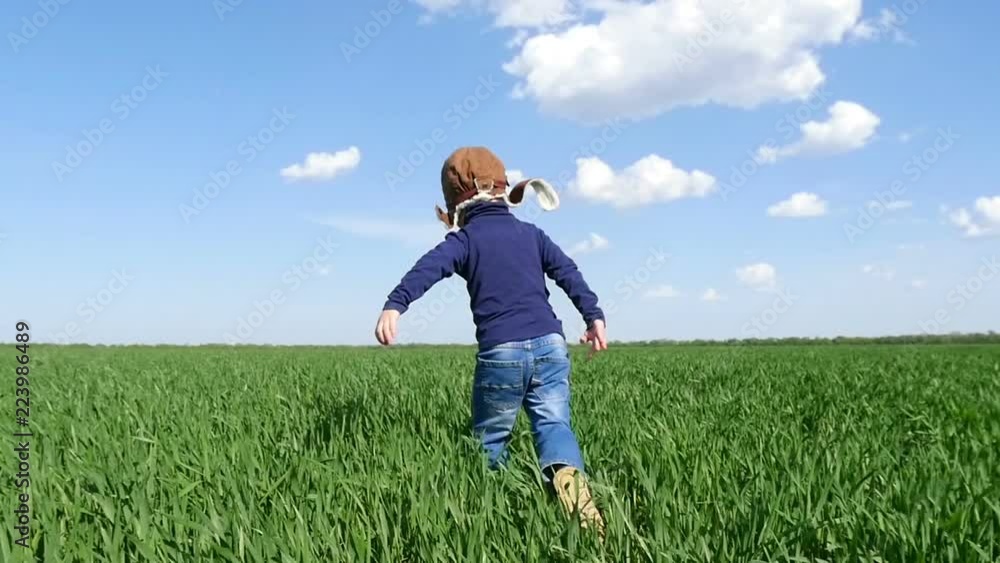 A happy child in a pilot's suit runs along a green field, in a slow motion.