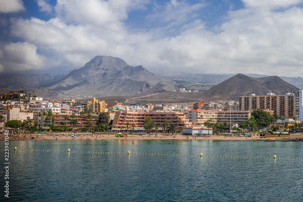 Los Cristianos coastline with white sand beach and cityscape with blue sky and clouds