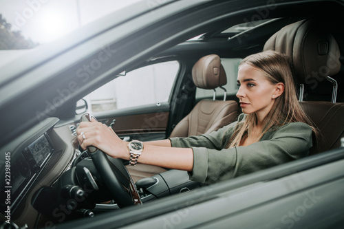 Side view focused woman holding steering wheel while sitting in cozy salon of automobile. Undistracted girl going at work concept