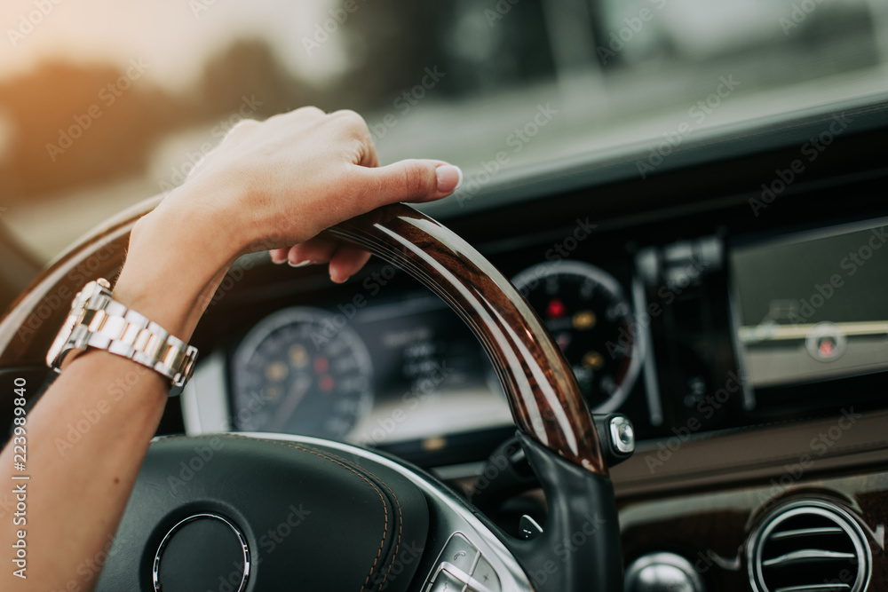 Close up female hand holding steering wheel while driving car. She wearing modern watch