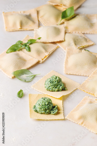 Homemade raw uncooked italian pasta ravioli staffed by spinach ricotta over white marble background. Close up, space