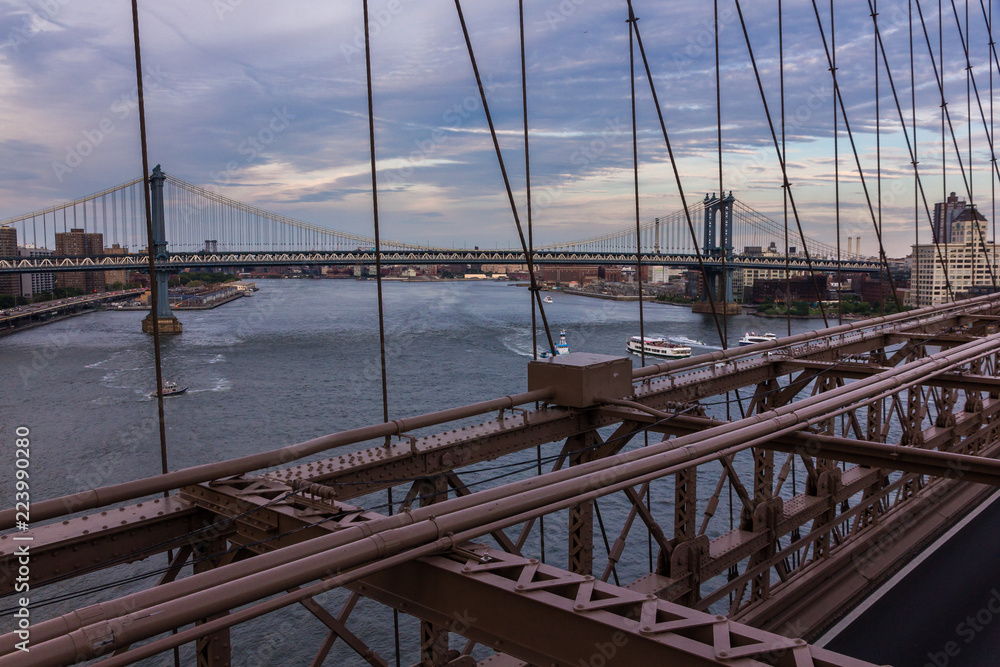 Manhattan Bridge viewed from Brooklyn Bridge at dusk, with some boats on the East River (New York, USA)