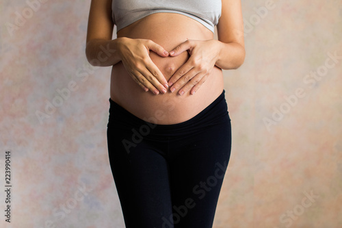 Pregnant Woman holding her hands in a heart shape on her baby bump. Pregnant Belly with fingers Heart symbol. Maternity concept. Baby Shower. toned
