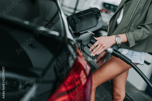 Close up woman hand holding the petrol pump nozzle while refueling the contemporary auto in petrol cap