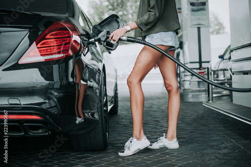 Woman in short shorts and white trainers servicing the modern vehicle while situating near it outdoor