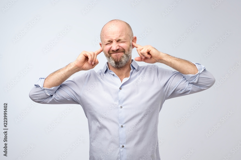 Annoyed mature man plugging ears with fingers Annoyed mature man plugging ears with fingers