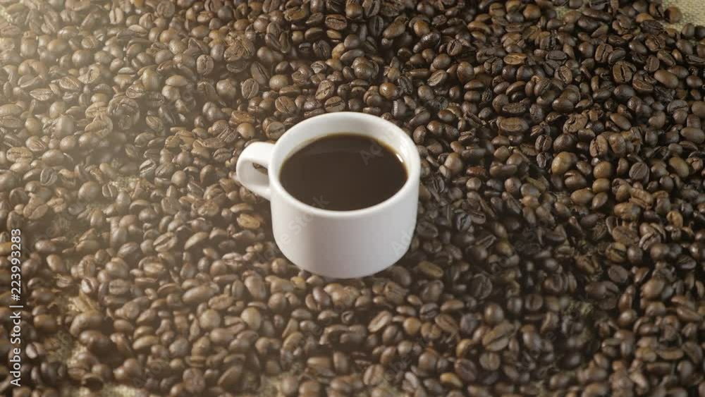 Coffee Cup and coffee beans. Women's hands draw a heart of coffee beans. A white Cup of steaming coffee with roasted beans around it. Coffee Cup and coffee beans. Women's hands draw a heart of coffee beans. A white Cup of steaming coffee with roasted beans around it.