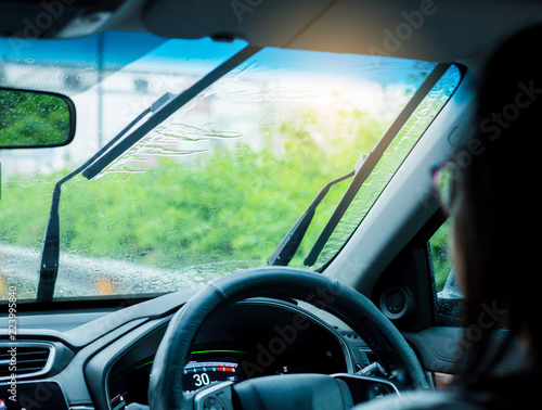 Selective focus of woman driving a car with rain droplet on windshield and wiper. © Koonsiri