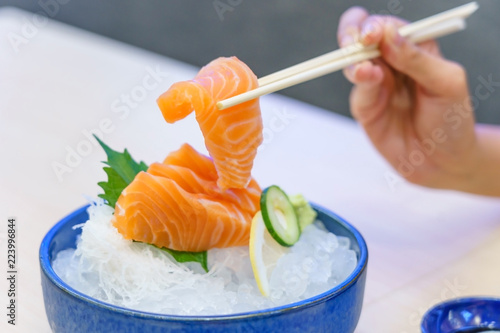 Hand holding salmon sashimi using chopsticks - Raw fresh salmon sliced served on ice with wasabi, Japanese food style.