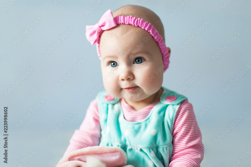 Pretty Baby Girl With Sweet Cute Pink Cheeks Child Has Blue Eyes Headband With Bow Little Baby Is Wearing In Children Dress And Clothes Blue Light Background Stock Photo Adobe Stock
