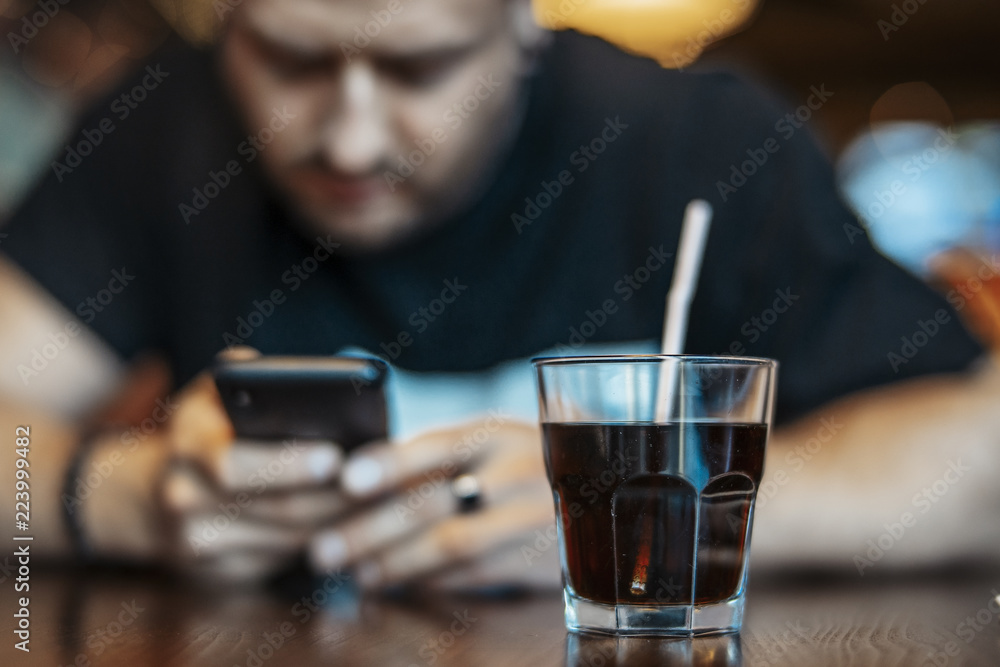 Young attractive man looking at mobile phone screen and drinking soda.