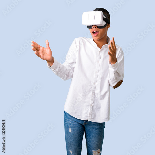 Young african american man with white shirt using VR glasses. Virtual reality experience on isolated blue background