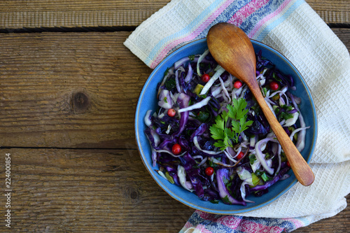 Stewed purple cabbage with parsley and cowberry on grey plate on wooden background. Vegan food. Healthy diet concept. Copy space.
